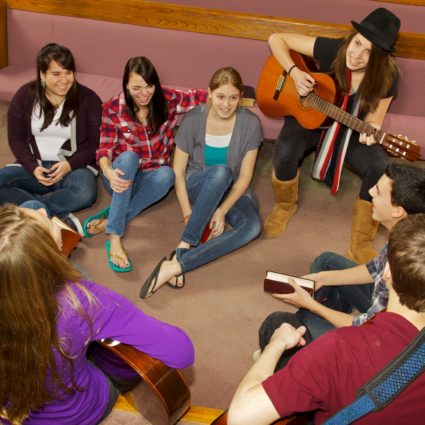 Happy Church Youth Group Eight teen friends play guitar and worship together in church setting