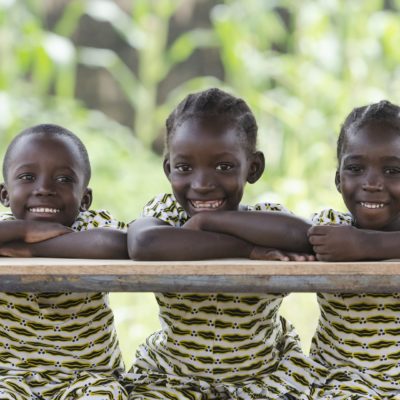 Three African Children at School Education Symbol Schoolgirl Schoolboy Sitting Three African children proudly sitting in their desk at school in Bamako, Mali. Candid outdoor shot of one boy and two girls learning their lessons at school.