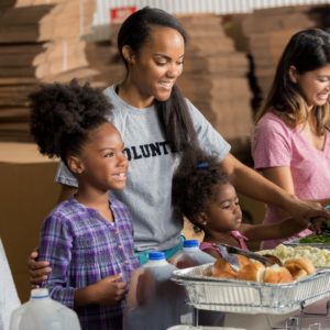 Diverse family volunteers together in soup kitchen African American mother and her two daughters serve meals to the homeless with their diverse family.